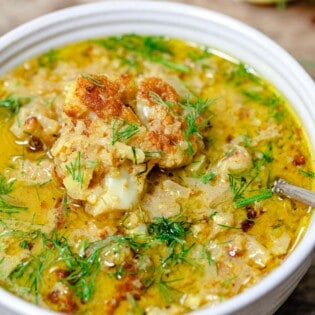 a close up of roasted cauliflower soup in a bowl with a spoon garnished with dill.