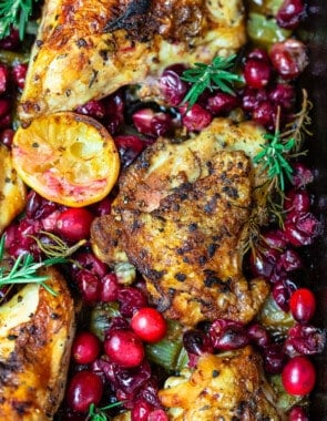 a close up of baked cranberry chicken topped with fresh cranberries, sprigs of fresh rosemary and lemon slices.