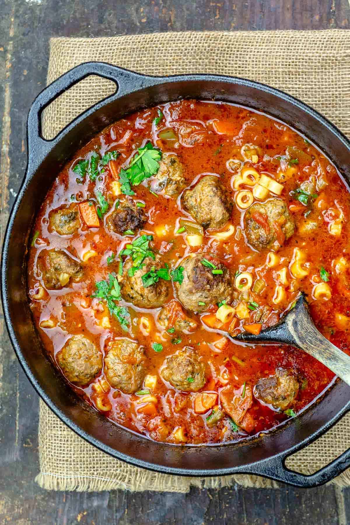 a large pot of meatball soup with a wooden serving spoon.