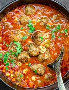 a large pot of meatball soup with a wooden serving spoon.