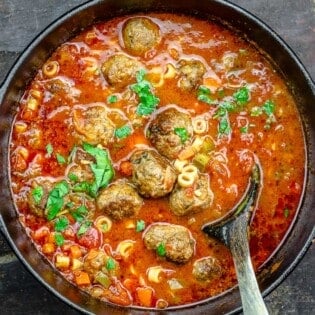 a large pot of meatball soup with a wooden serving spoon.