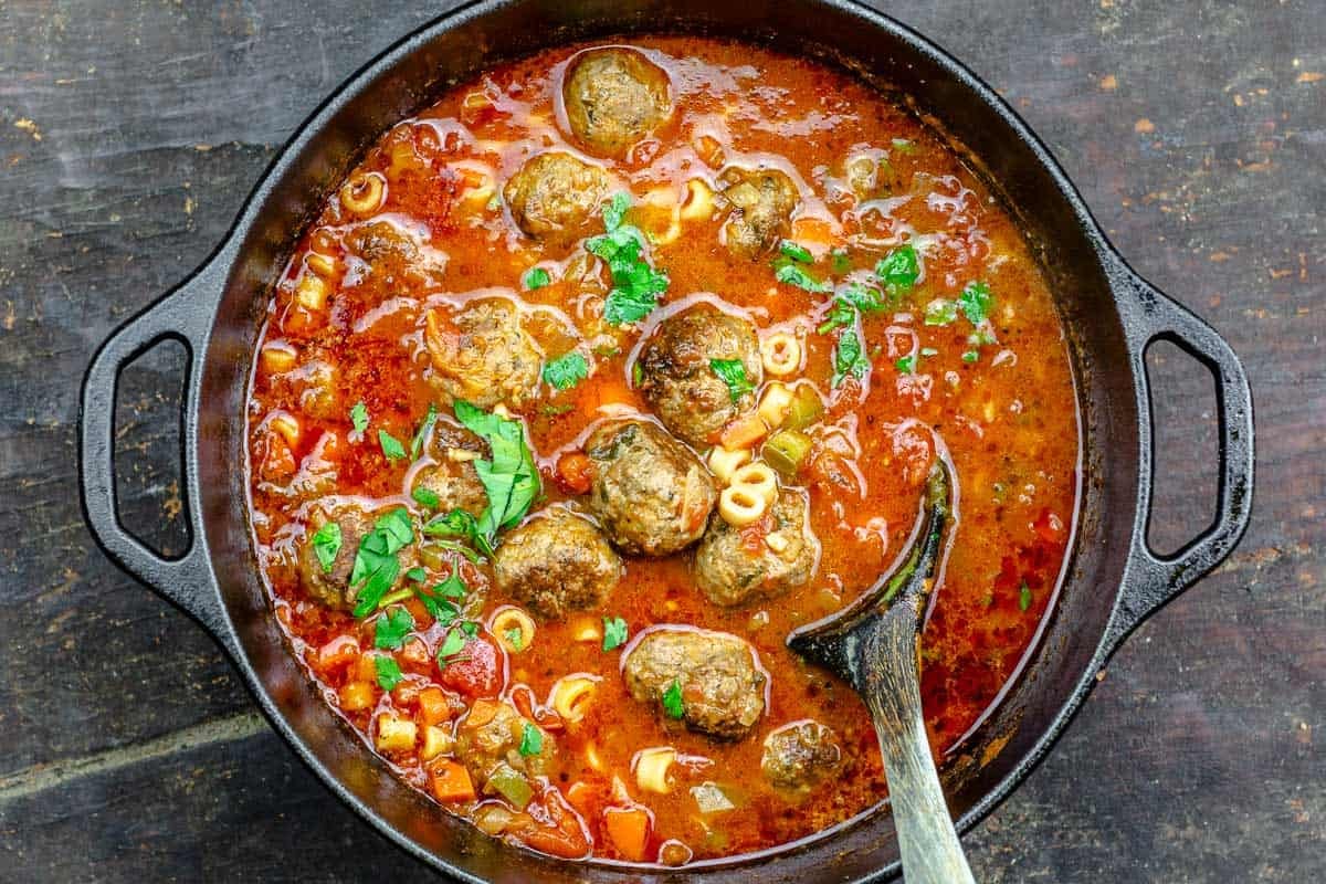 a large pot of meatball soup with a wooden serving spoon.