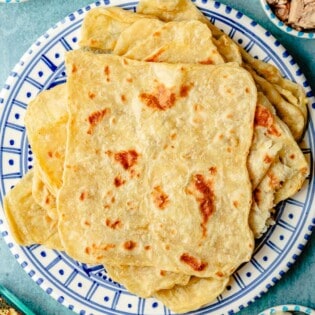 mlewi flatbreads stacked on a plate, surrounded by small bowls of olives, hard boiled eggs, tuna, cream cheese, harissa and a dish of homemade oven fries.