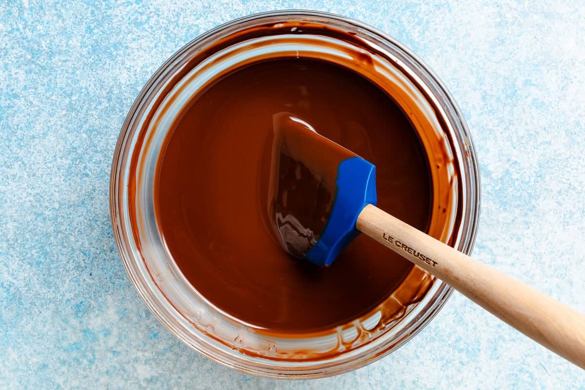 Melted chocolate and olive oil that have been stirred in a glass bowl with a rubber spatula until smooth.