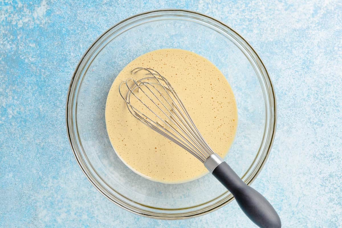 Egg yolks, sugar, salt, vanilla extract, lemon zest, and coffee in a glass bowl with a whisk.