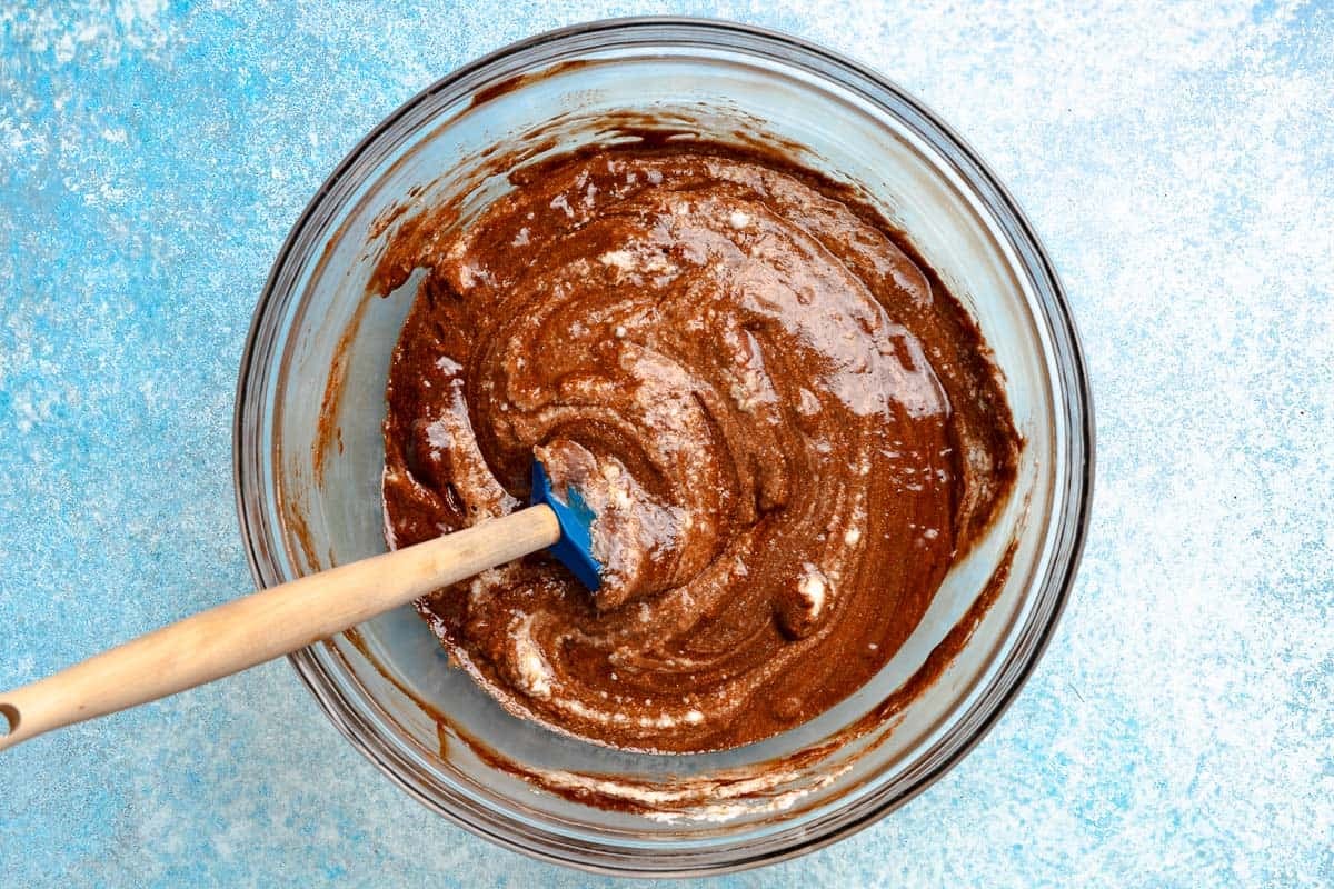 A glass bowl with a rubber spatula mixing the melted chocolate and egg yolk mixture.