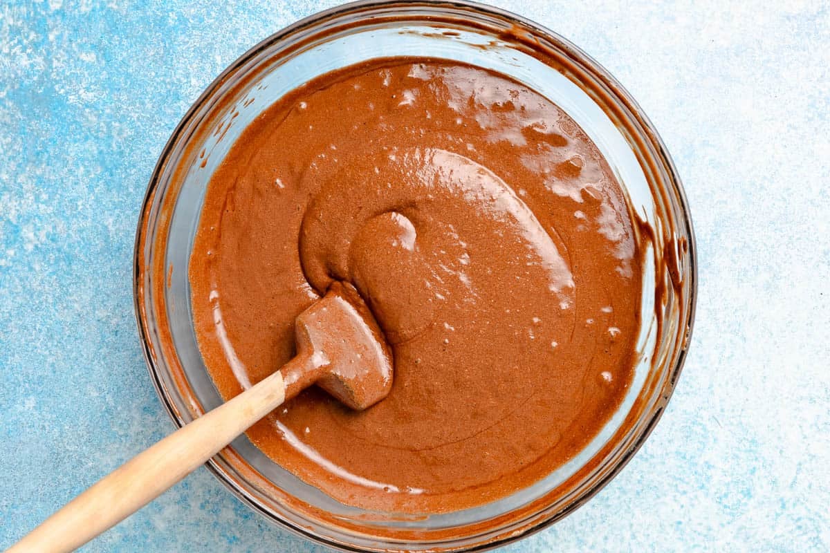 A glass bowl with a rubber spatula mixing the melted chocolate and egg yolk mixture together with the beaten egg white mixture.