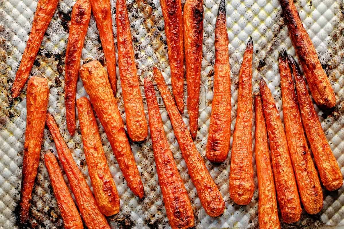 Carrots that have been roasted on a sheet pan, showing their charred tips and browned spots.