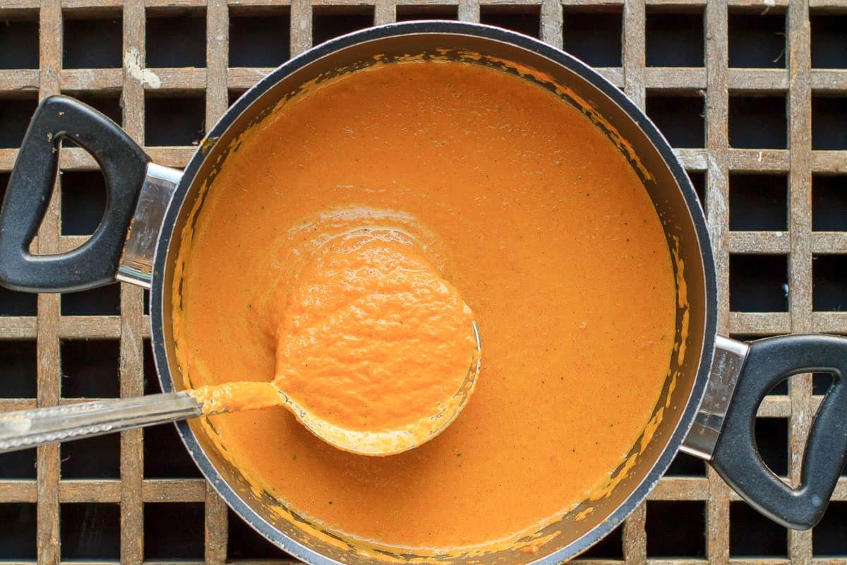 Metal ladle showing the texture of roasted carrot soup. It's nice and thick with some texture.