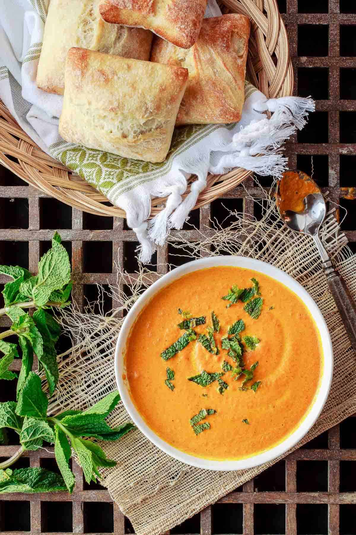 Overhead shot of roasted carrot soup in a bowl with ciabatta bread on the side.