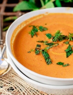Carrot soup in a white bowl with fresh mint on top.
