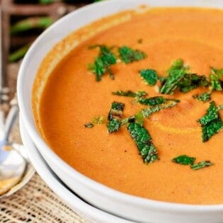 Carrot soup in a white bowl with fresh mint on top.