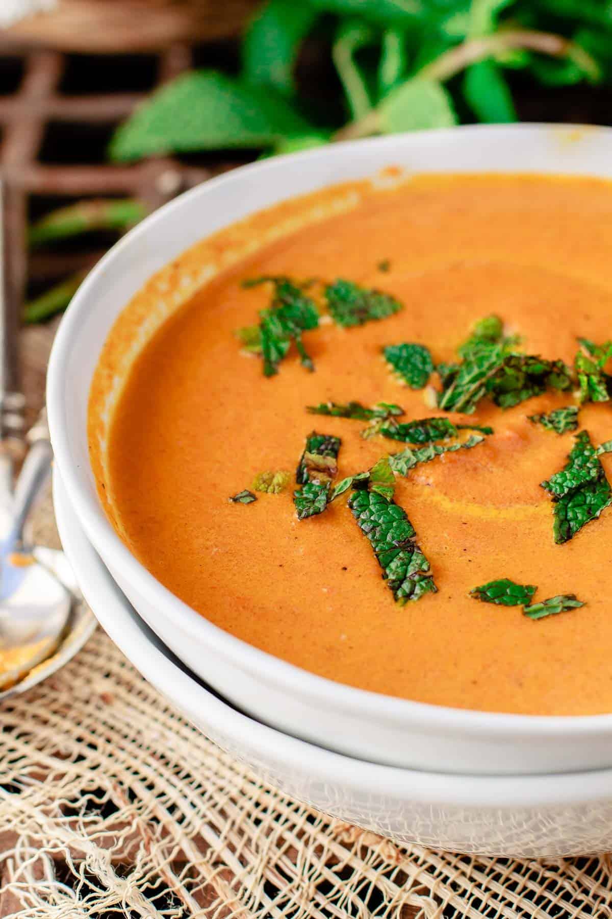 Carrot soup in a white bowl with fresh mint on top.