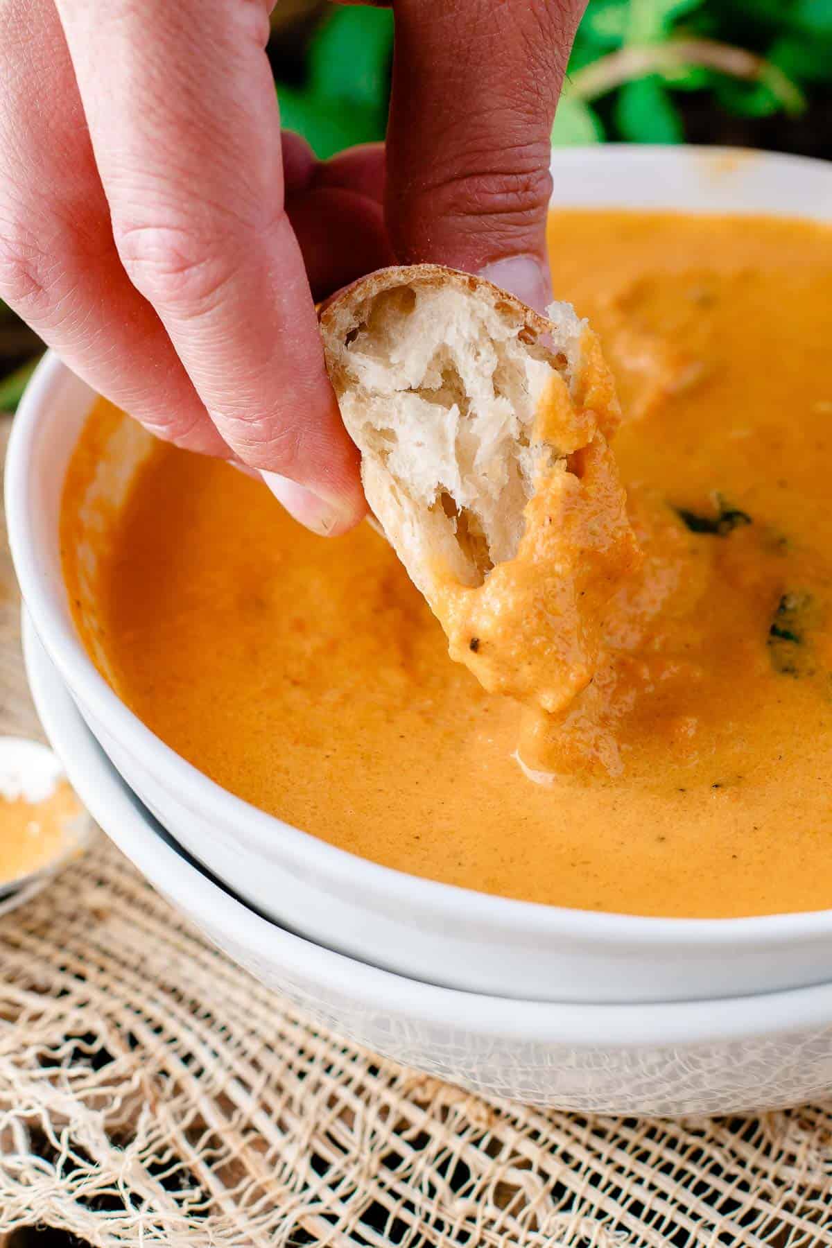 Person dipping a piece of bread into carrot soup.