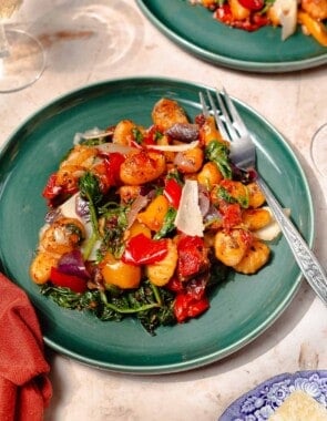 a serving of sheet pan gnocchi on a teal plate with a silver fork and white wine on the side.