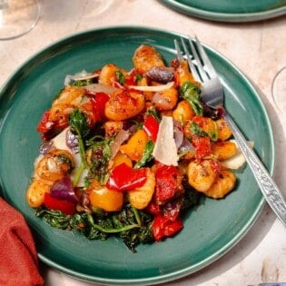 a serving of sheet pan gnocchi on a teal plate with a silver fork and white wine on the side.