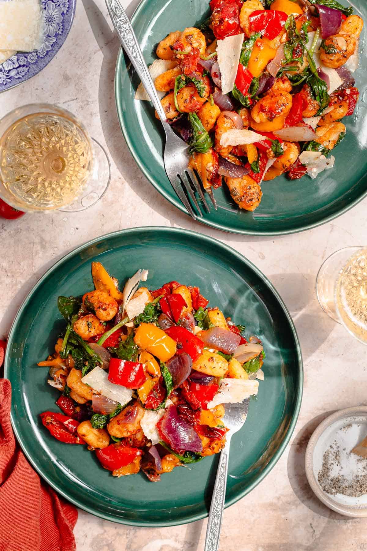 Sheet pan gnocchi with roasted bell pepper, red onion, cherry tomatoes, herbs, and parmesan shavings on a teal plate.