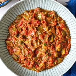 Overhead shot of taktouka in a blue bowl, showing the jammy tomatoes and oil around the edges.