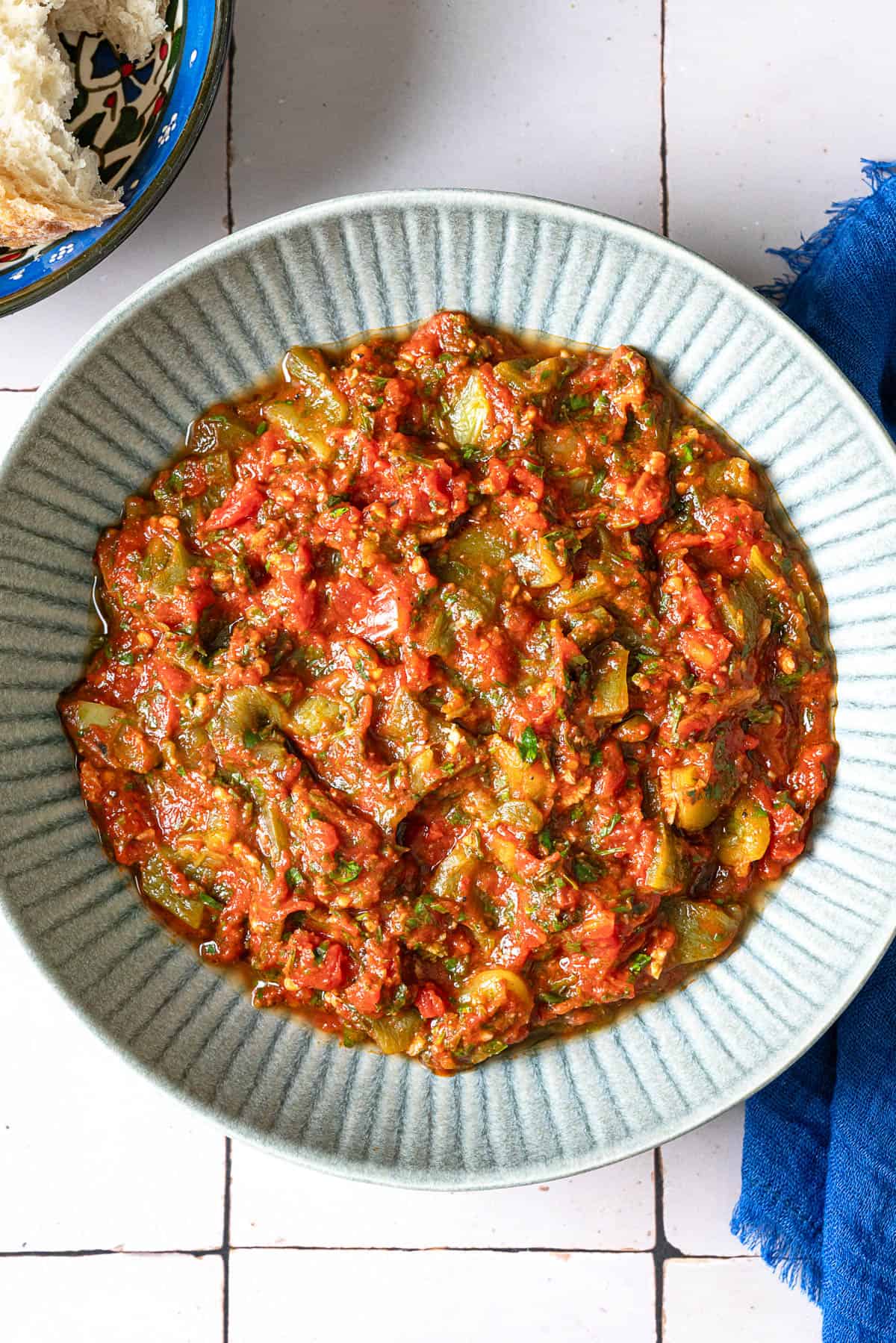 Overhead shot of taktouka in a blue bowl, showing the jammy tomatoes and oil around the edges.