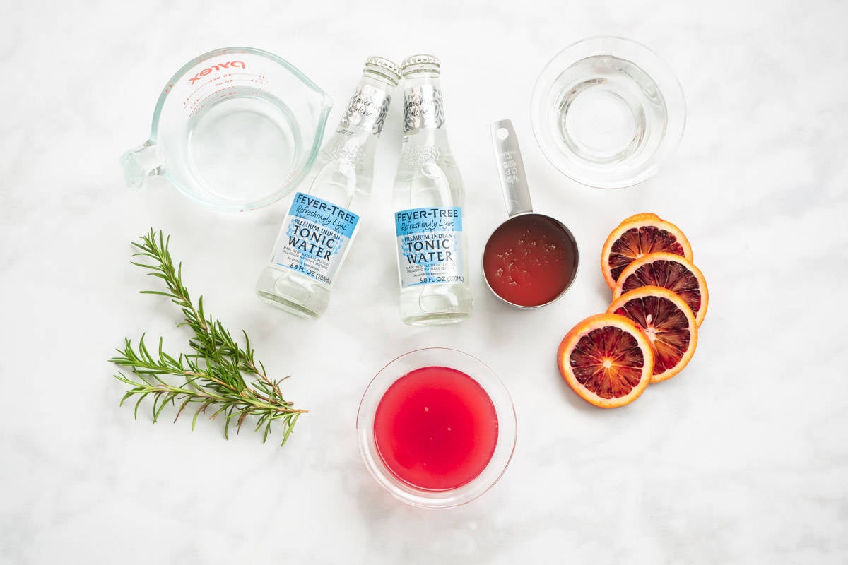 ingredients for blood orange rosemary cocktail including tonic water, honey, blood oranges, rosemary, vodka, and blood orange rosemary syrup.