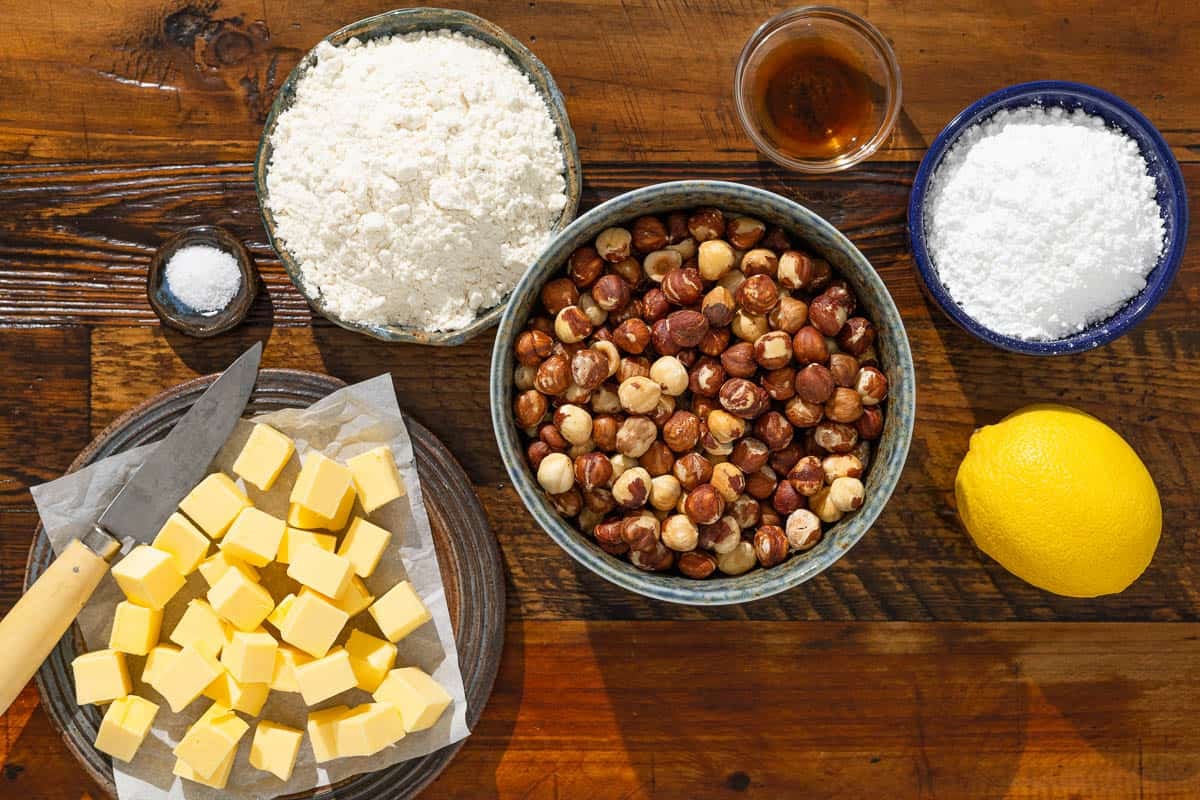 ingredients for baci di dama hazelnut cookies including hazelnuts, powdered sugar, flour, salt, butter, vanilla extract, and lemon.