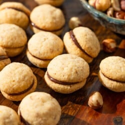 a close up of baci di dama hazelnut cookies placed on a table next to a bowl of hazelnuts.