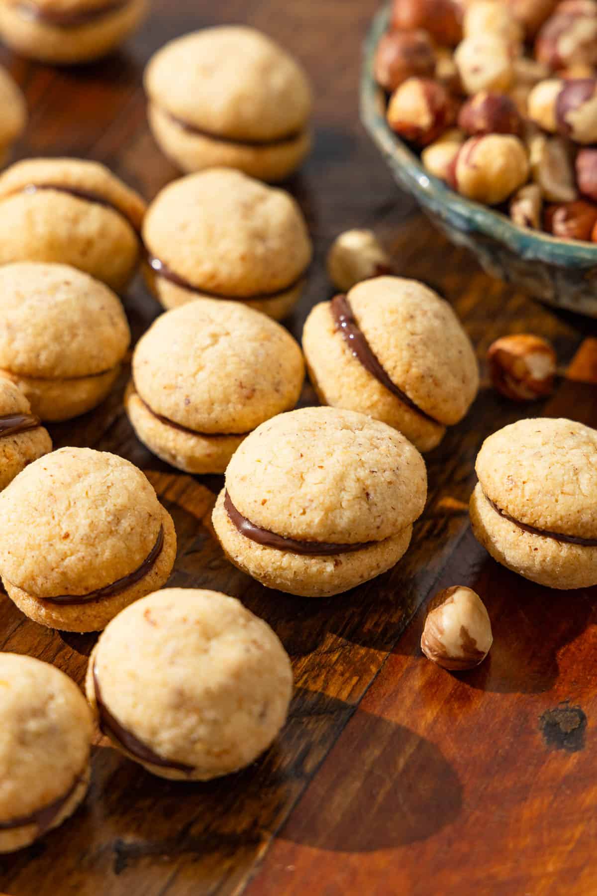 a close up of baci di dama hazelnut cookies placed on a table next to a bowl of hazelnuts.