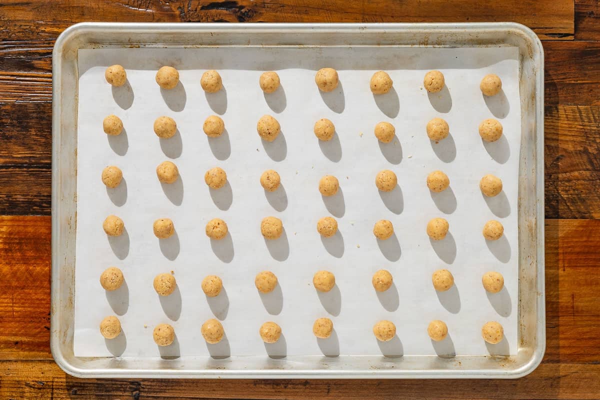 unbaked baci di dama hazelnut cookie dough balls spread out on a parchment lined baking sheet.