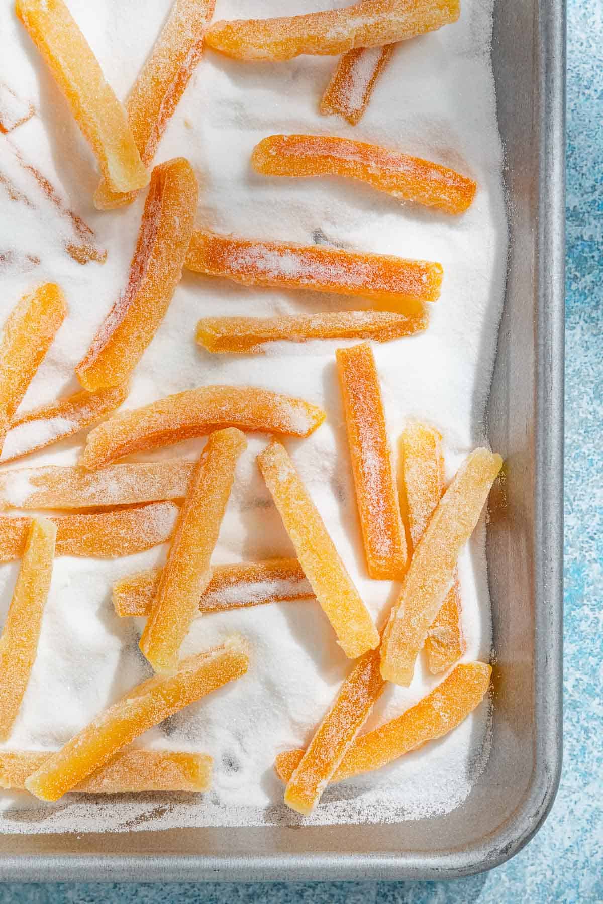 an overhead photo of candied orange peels being coated in sugar in a sheet pan.