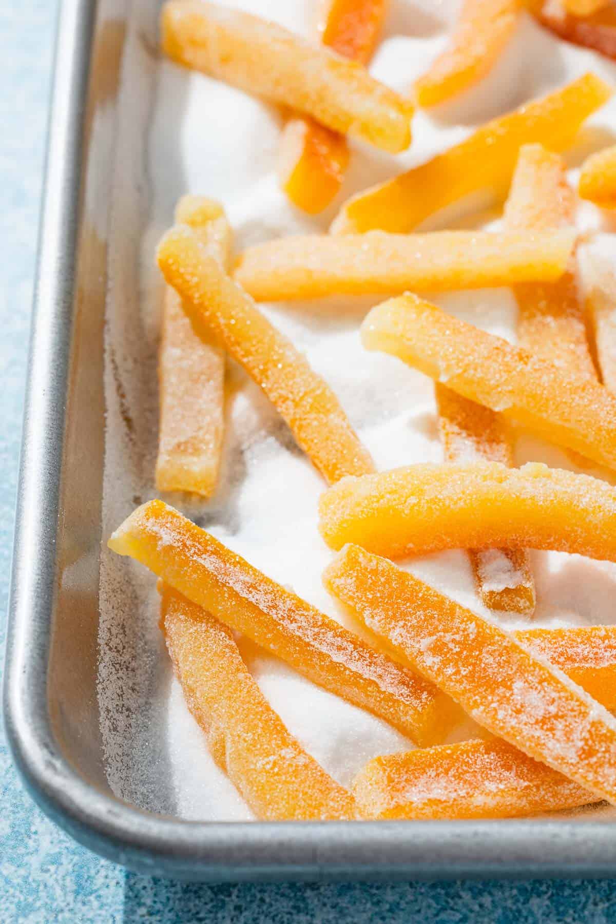 a close up of candied orange peels being coated in sugar in a sheet pan.