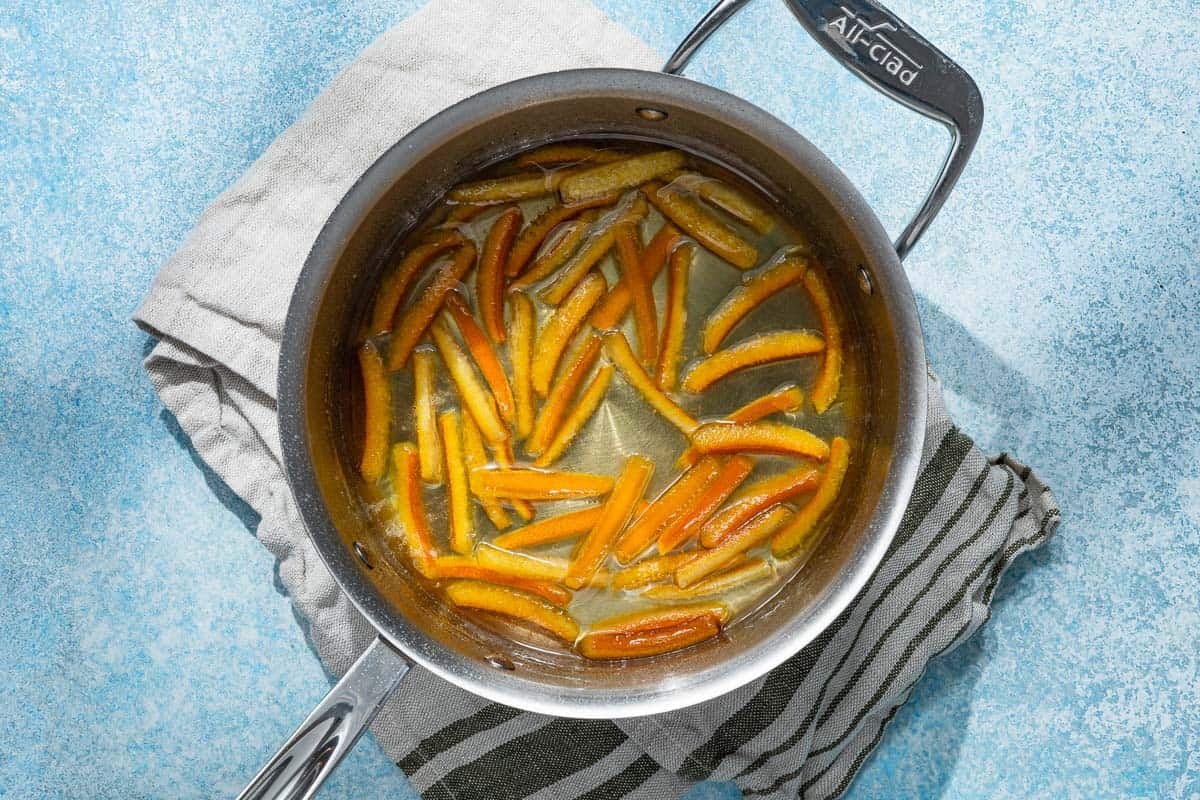 orange peels being candied in a sauce pan of sugar syrup.