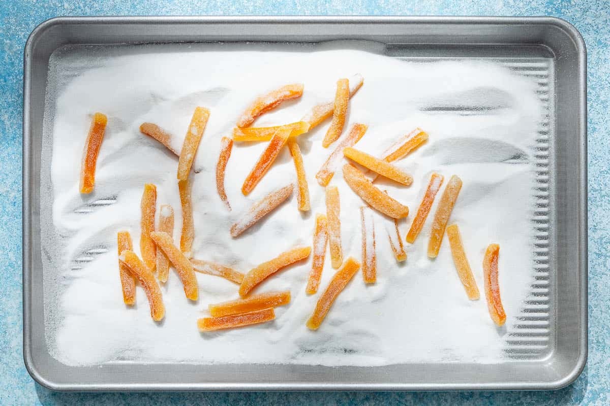 an overhead photo of candied orange peels being coated in sugar in a sheet pan.