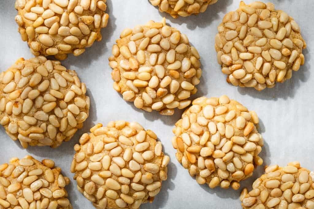 an overhead photo of several baked pignoli cookies on parchment paper.