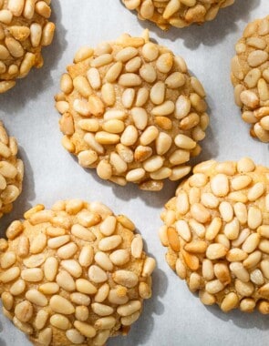 an overhead photo of several baked pignoli cookies on parchment paper.