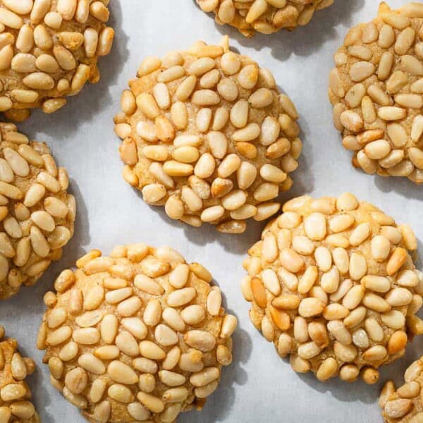 an overhead photo of several baked pignoli cookies on parchment paper.