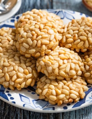 a close up of several pignoli cookies stacked on a serving plate.