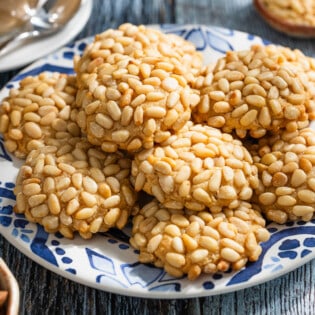 a close up of several pignoli cookies stacked on a serving plate.