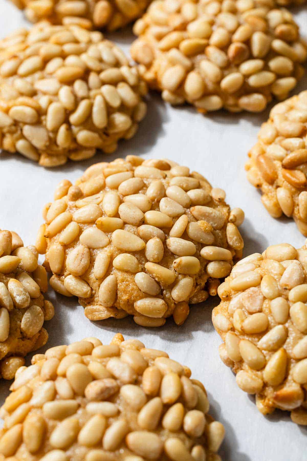 a close up of several baked pignoli cookies on parchment paper.