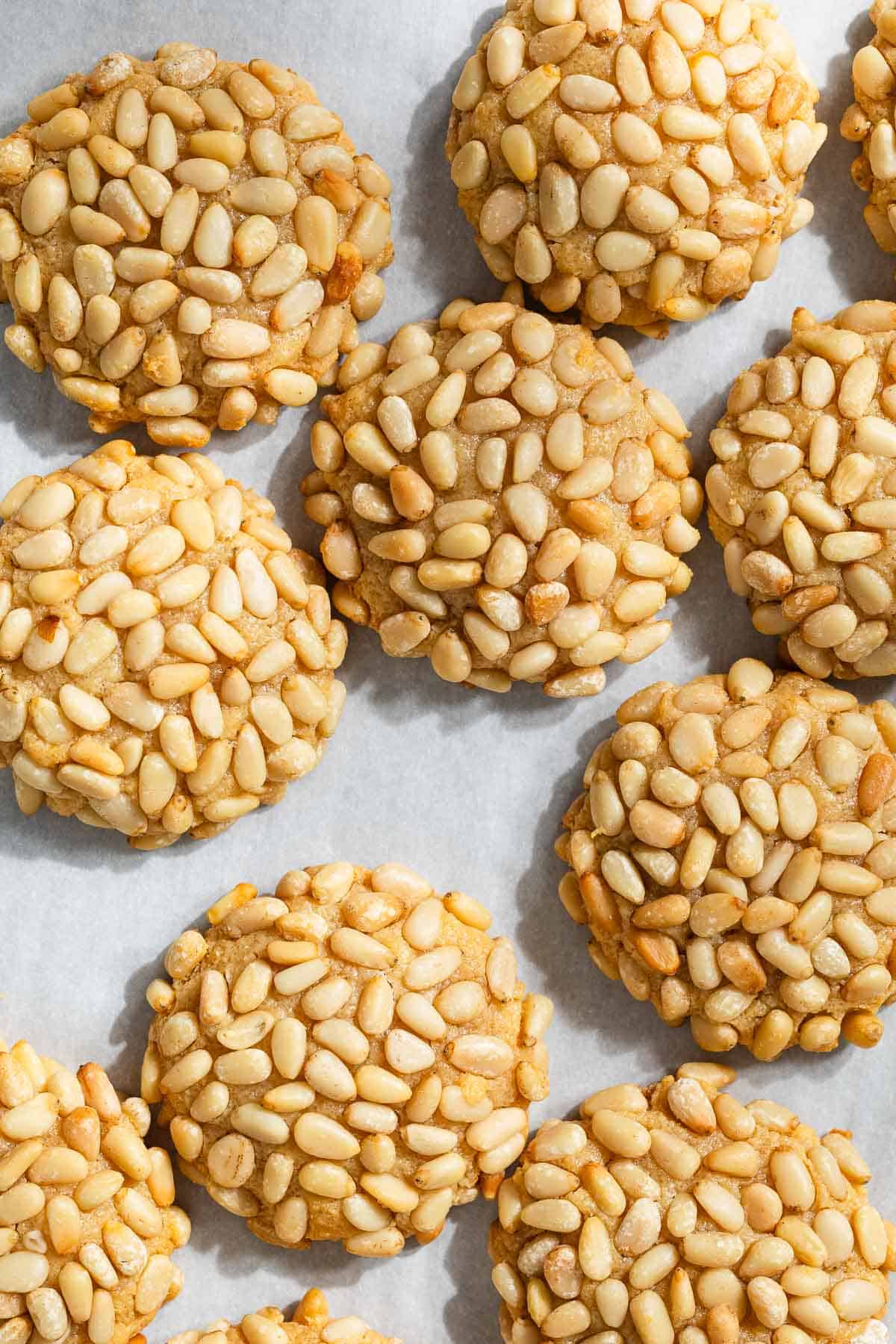 a close up of several baked pignoli cookies on parchment paper.