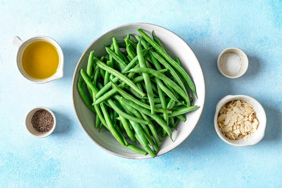 ingredients for roasted green beans including fresh green beans, olive oil, kosher salt, black pepper, and sliced almonds.