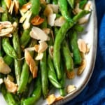 a close up of a platter of roasted green beans garnished with sliced almonds.