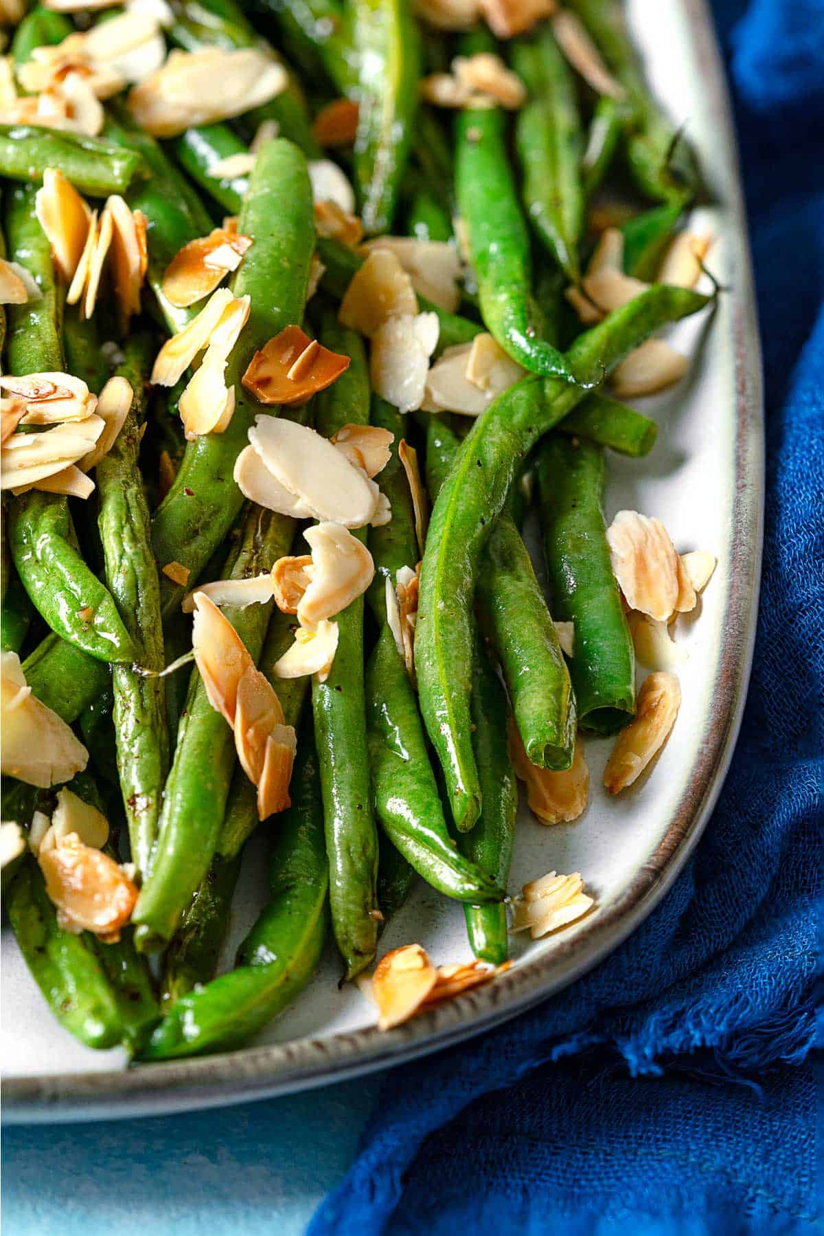 a close up of a platter of roasted green beans garnished with sliced almonds.