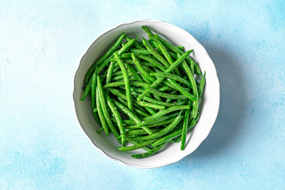 fresh green beans in a white bowl seasoned with salt and pepper.