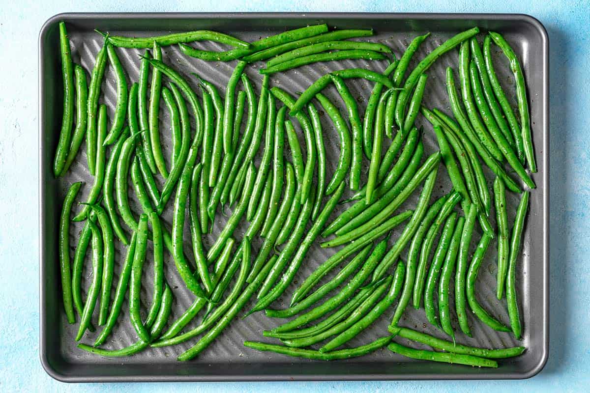 seasoned green beans spread evenly on a baking sheet.