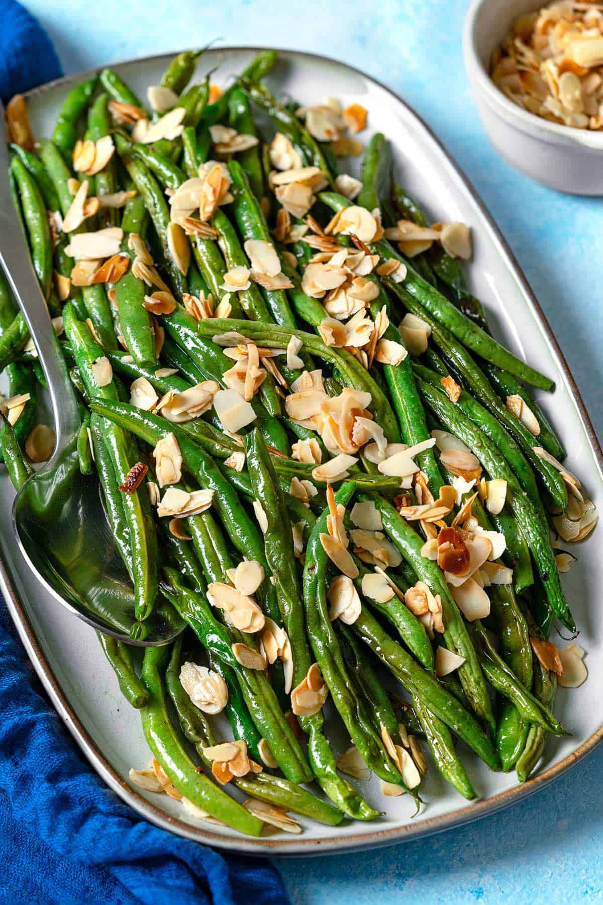 a serving platter of roasted green beans garnished with sliced almonds with a serving spoon.