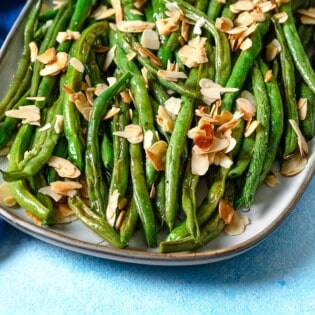 a close up of a serving platter of roasted green beans garnished with sliced almonds.