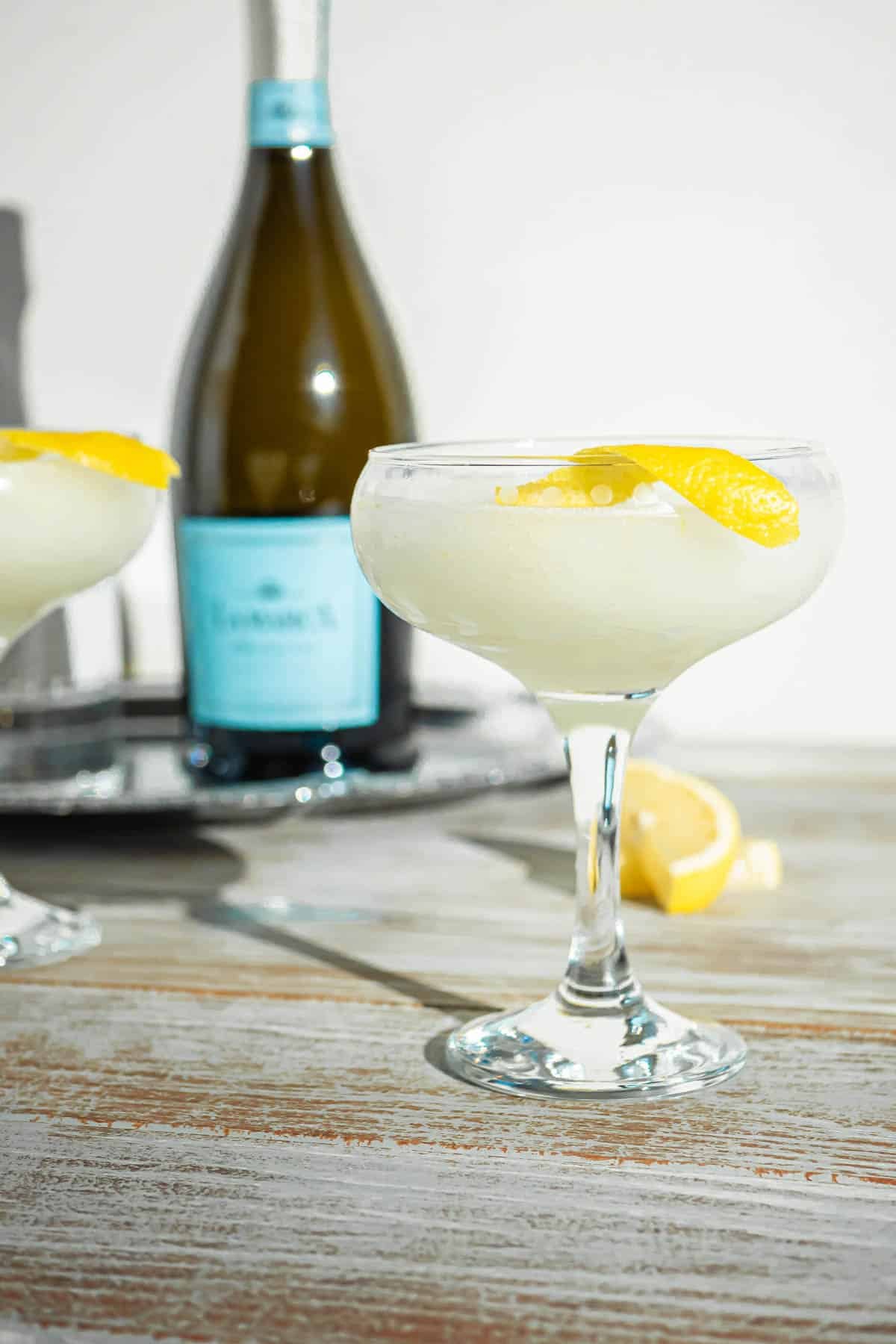 a sgroppino prosecco cocktail garnished with a lemon peel in front of a tray with a bottle of prosecco.