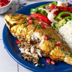 A serving of persian baked fish on a plate with rice and a salad. A part of the fish has been cut open showing the stuffing inside.