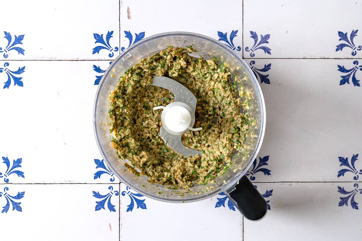 walnuts, aromatics, green olives, pomegranate molasses and olive oil mixed into a paste inside the bowl of a food processor.