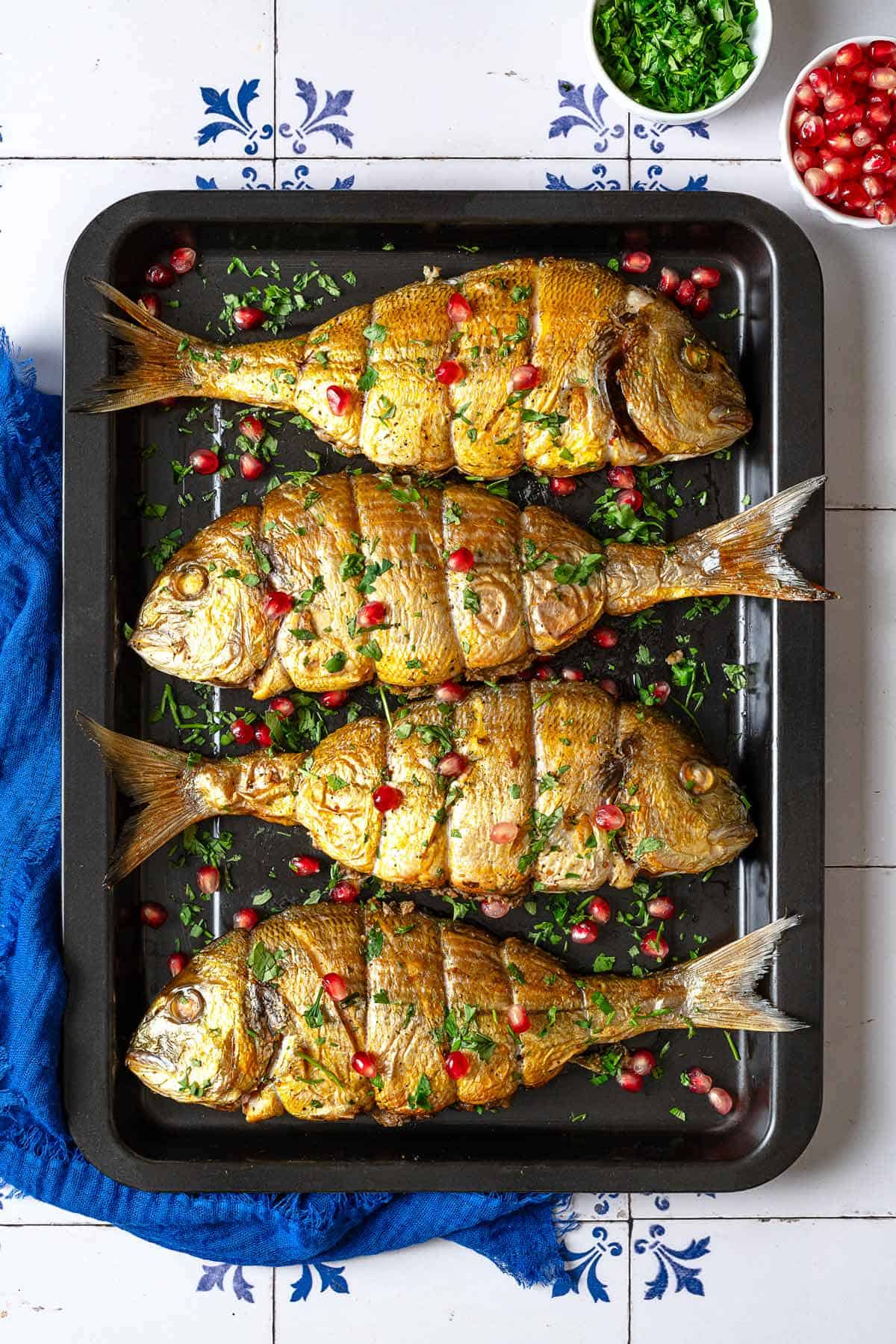 an overhead photo of 4 cooked persian baked fishes garnished with pomegranate seeds and parsley on a sheet pan.